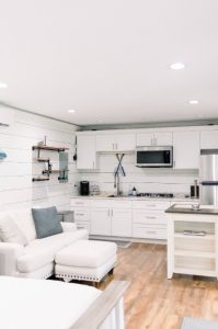 white studio with kitchen cabinets in background and foot of bed in the foreground, wood floors