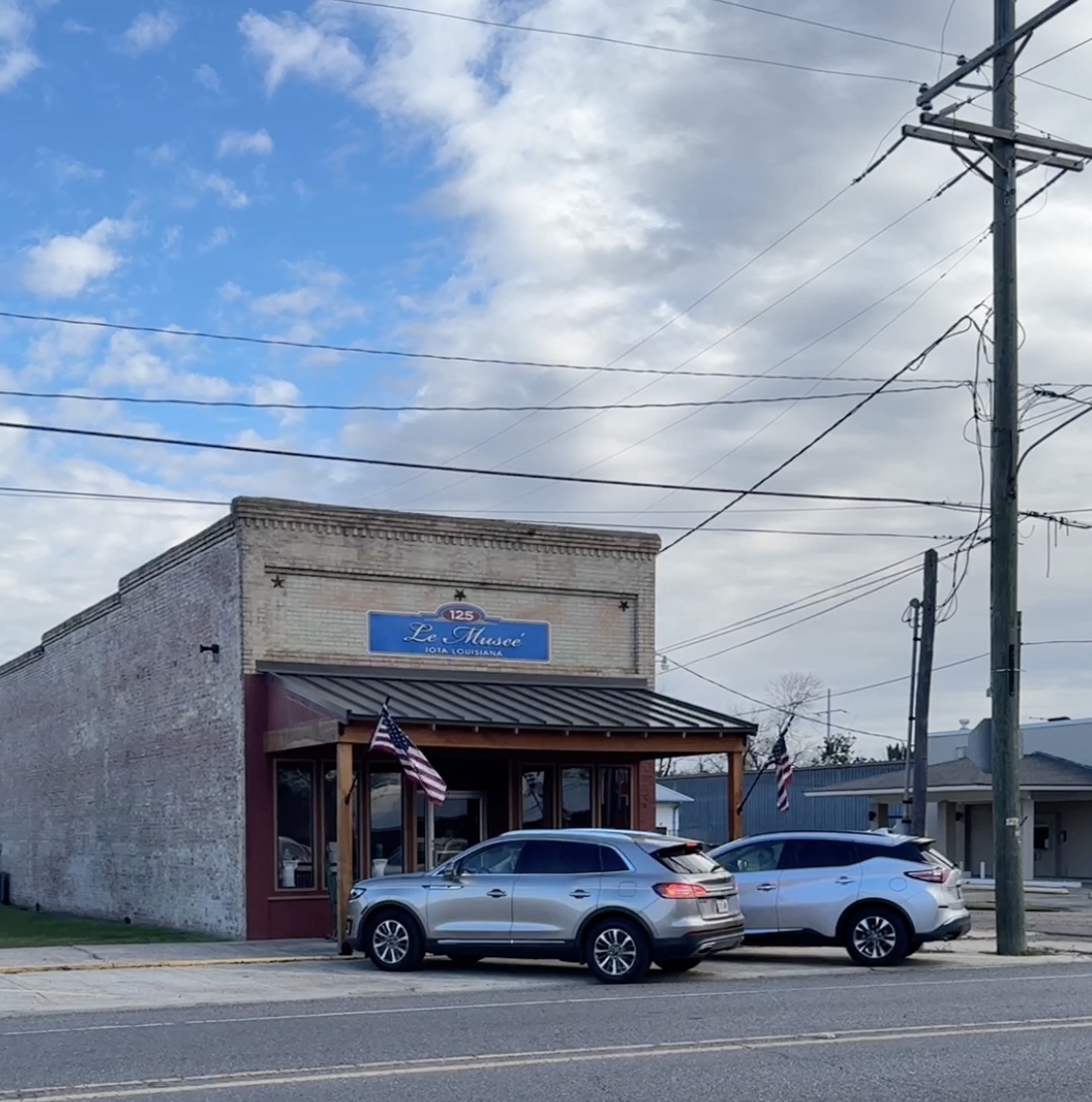 front of historic brick building with porch and two cars parked in front
