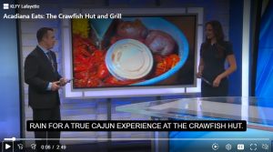 News reporter standing in the studio in front of a monitor featuring a picture of a tray of crawfish