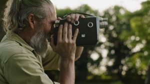 Man looking through the lens of a video camera with trees in the background