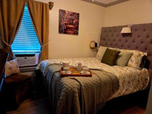 Bedroom with bed with tufted headboard, hospitality tray laid, out, curtains, and window AC unit