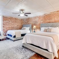 bedroom with two beds with tufted headboards, large area rug, and exposed brick walls