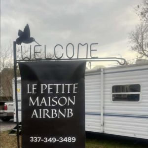 Black welcome flag promoting Le Petite Maison AirBNB with a camper in the background
